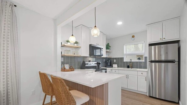 A modern kitchen with a central island, stainless steel appliances, and a dining area with wicker chairs.