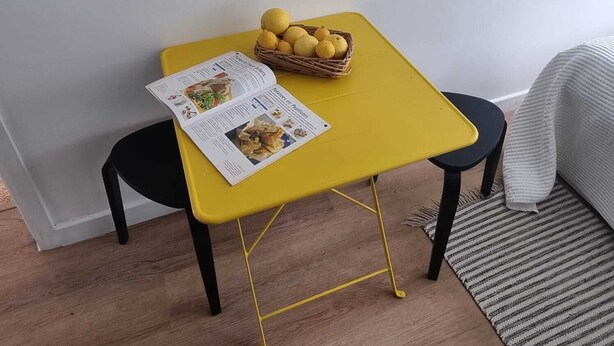 A small yellow table with a basket of lemons and a menu on it, flanked by two black chairs. - Yellow Studio - Wembley Stadium - London (Wembley)