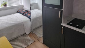A compact kitchenette with a built-in oven and microwave, a small dining area with a yellow chair, and a window with blinds. - Yellow Studio - Wembley Stadium - London (Wembley)
