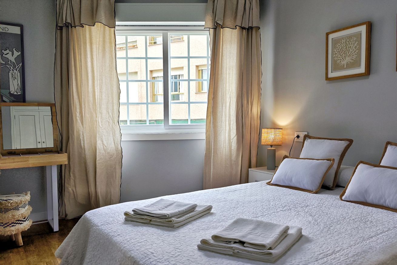 A hotel room with a bed, a nightstand, a lamp, a window with curtains, and a wall-mounted picture.