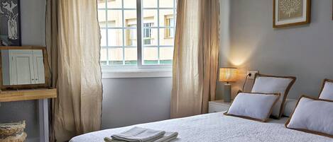 A hotel room with a bed, a nightstand, a lamp, a window with curtains, and a wall-mounted picture.