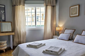 A hotel room with a bed, a nightstand, a lamp, a window with curtains, and a wall-mounted picture.