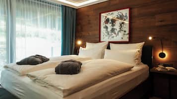 A double bed with white linens and two dark towels, a painting on the wall, and a bedside lamp.