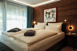 A double bed with white linens and two dark towels, a painting on the wall, and a bedside lamp.