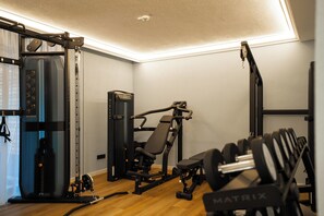 Un gimnasio con equipos de ejercicio variados, incluyendo una estructura para sentadillas, una prensa de banca y mancuernas.