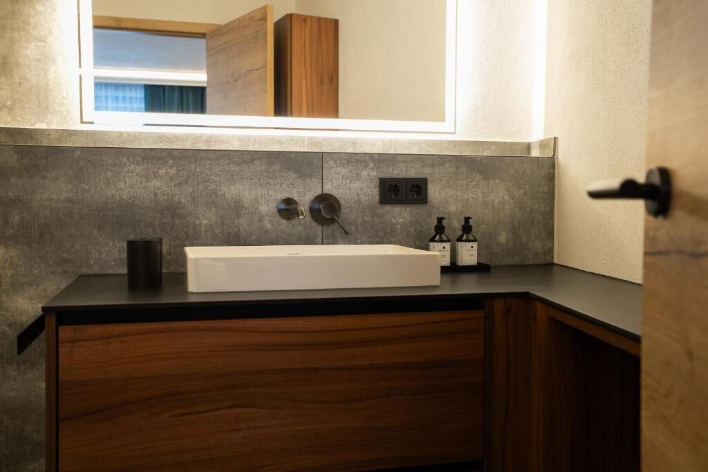 Un baño con lavamanos blanco, armarios de madera, un espejo y una ventana.