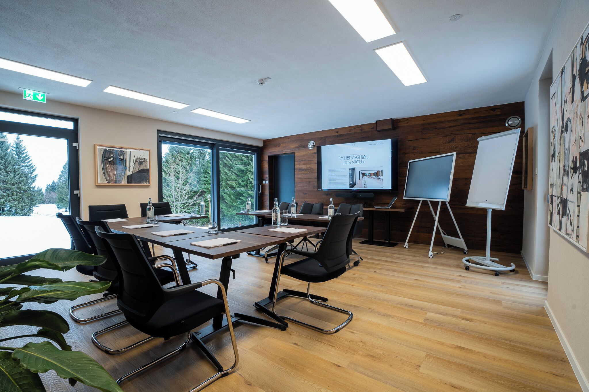 Sala de conferências com uma mesa grande, cadeiras, tela de projetor e quadro branco.