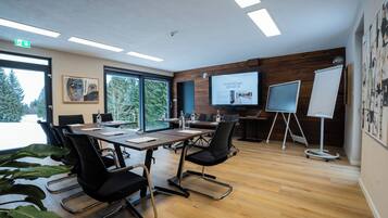 Sala de conferências com uma mesa grande, cadeiras, tela de projetor e quadro branco.