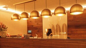 A reception desk with a wooden finish, multiple pendant lights, and a sign for 'Aler Bergwald Art Galleries'. - Allgäuer Bergwald Chalets  (Oberstaufen)