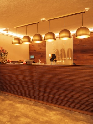 Un mostrador de recepción con detalles de madera, varias luces colgantes y un cartel para 'Aler Bergwald Art Galleries'.