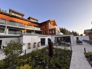 A modern building with a rooftop terrace, outdoor seating area, and a garden with various plants.