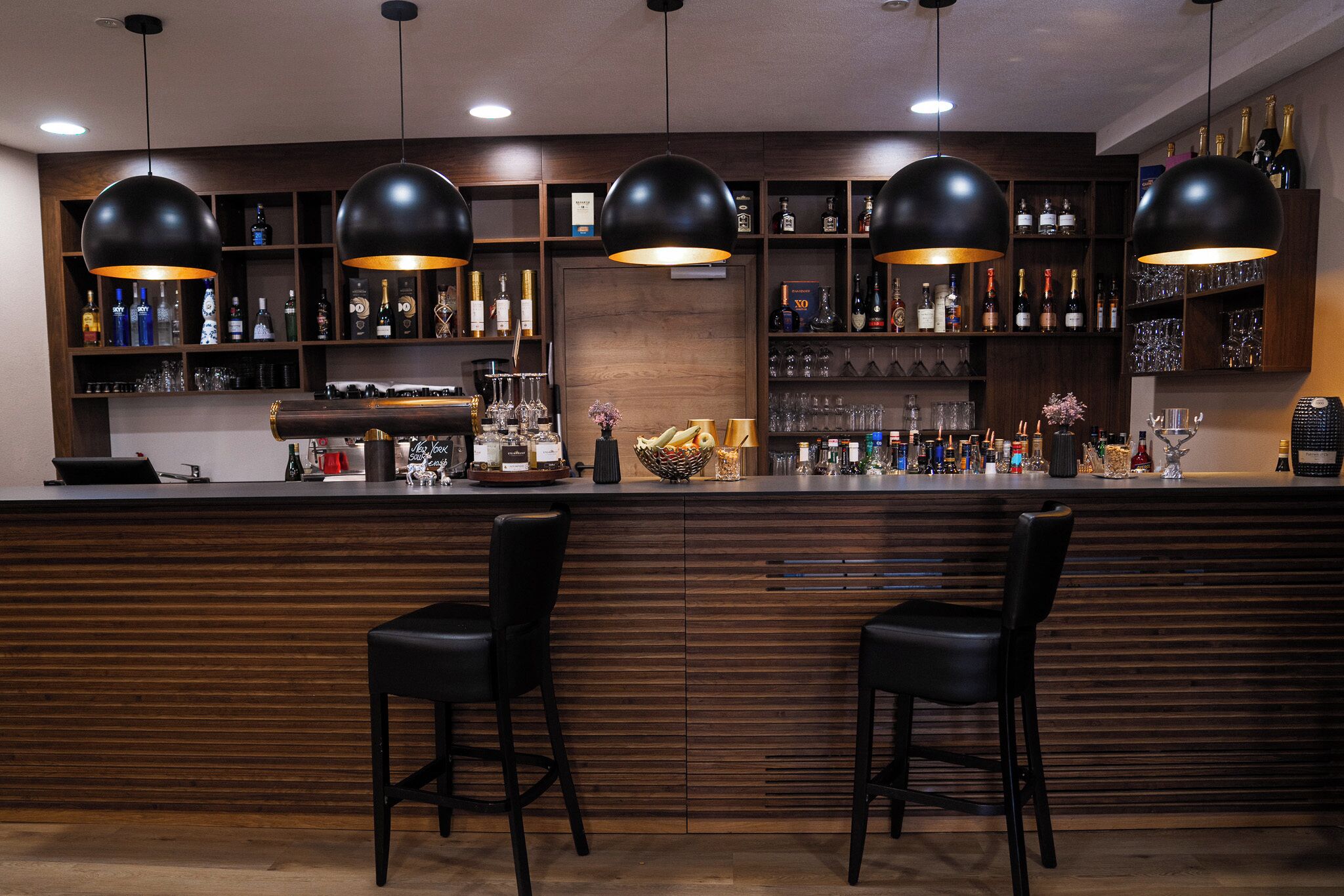 A bar area with wooden paneling, black bar stools, and pendant lighting.
