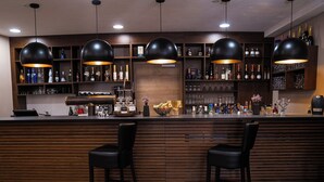 A bar area with wooden paneling, black bar stools, and pendant lighting. - Allgäuer Bergwald Chalets  (Oberstaufen)