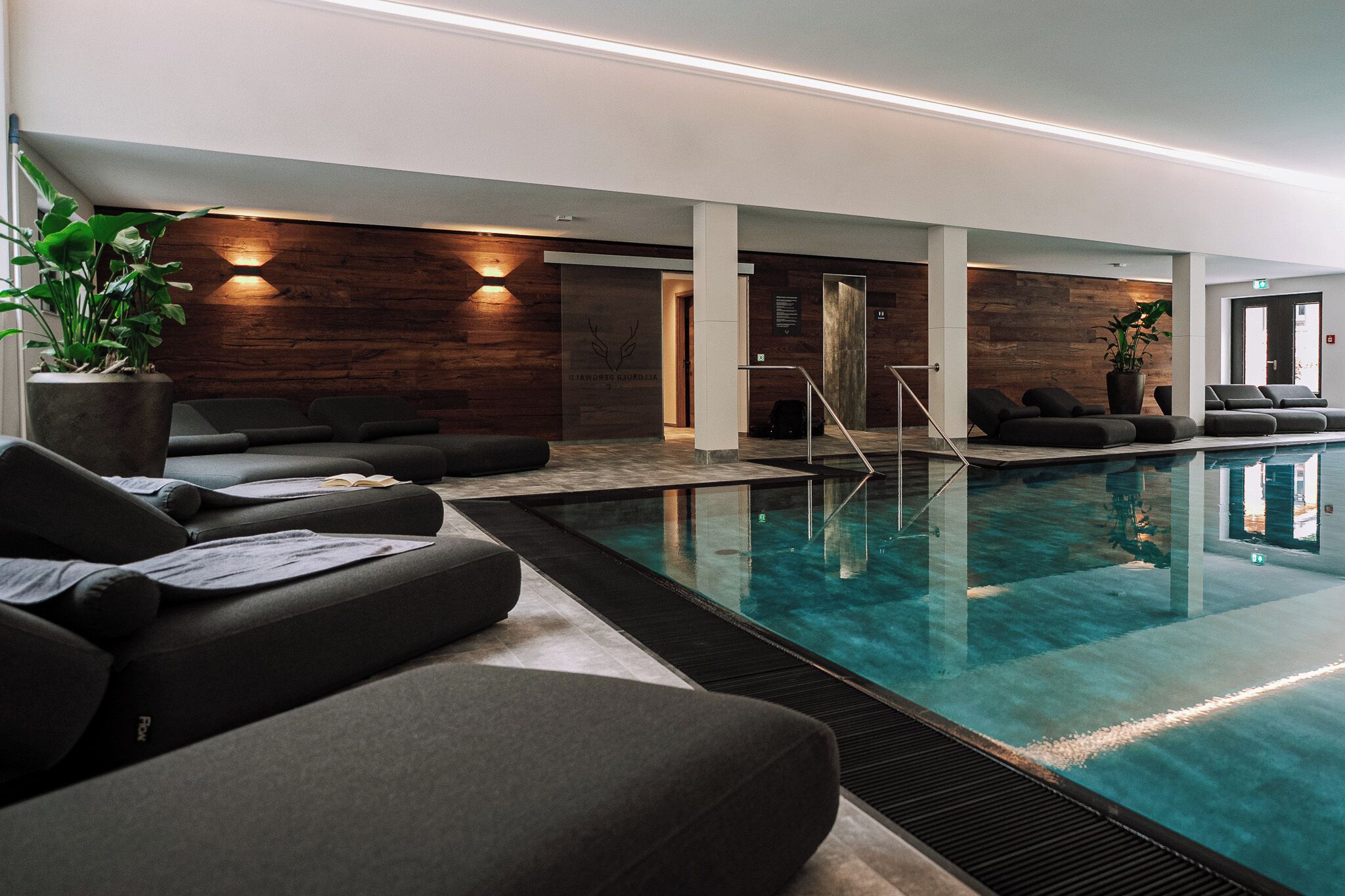 Una piscina interna moderna con poltroncine relax e una parete in legno.