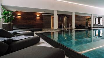 Una piscina interna moderna con poltroncine relax e una parete in legno.
