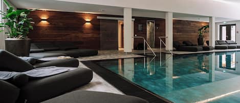 Une piscine intérieure moderne, dotée de chaises longues et d’un mur en bois.