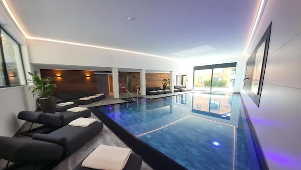 A modern indoor pool area with seating and a view of the outside. - Allgäuer Bergwald Chalets  (Oberstaufen)