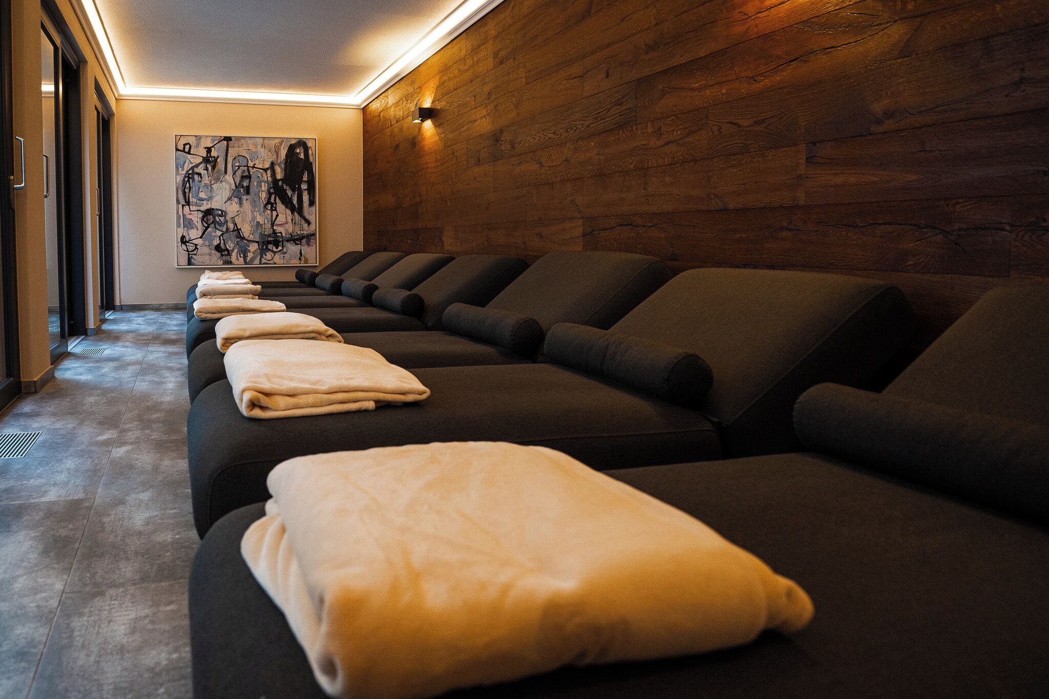 Eine Reihe dunkler Massagesitze mit Handtüchern, eine Holzwand und ein Gemälde an der Wand.