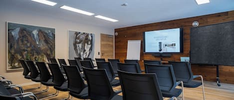Ein Konferenzraum mit Reihen schwarzer Stühle, einer großen Leinwand und Holzvertäfelung an den Wänden.