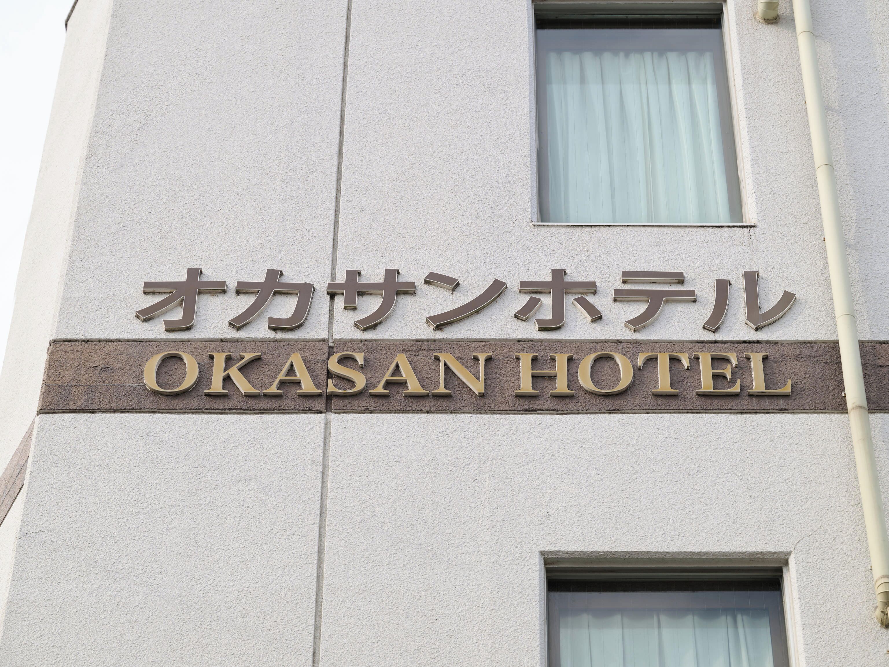 The exterior of the Okasan Hotel with its name displayed in both Japanese and English.