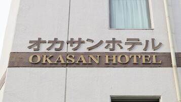 The exterior of the Okasan Hotel with its name displayed in both Japanese and English.