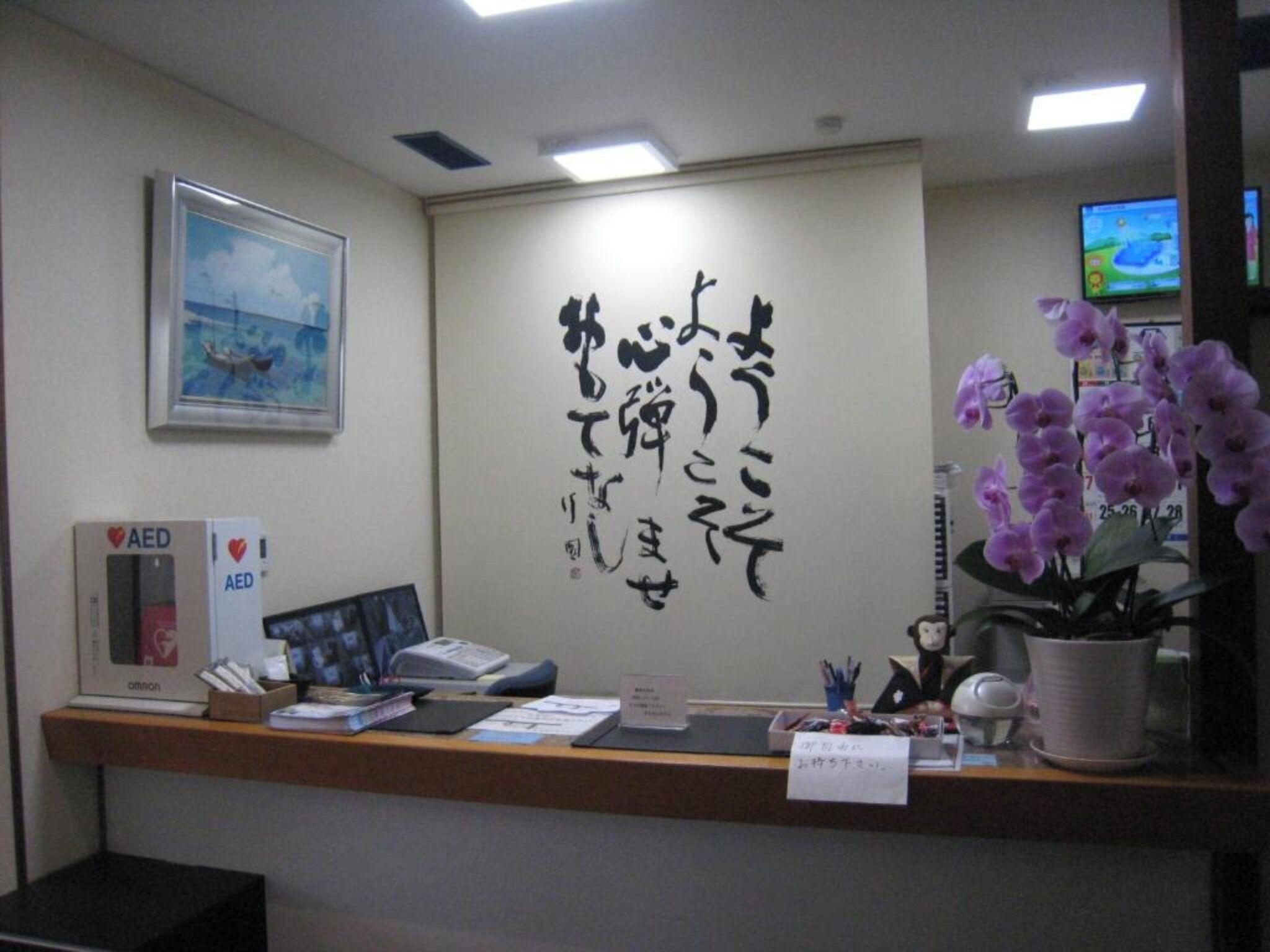 A reception desk with a framed picture, an AED box, and a potted orchid.