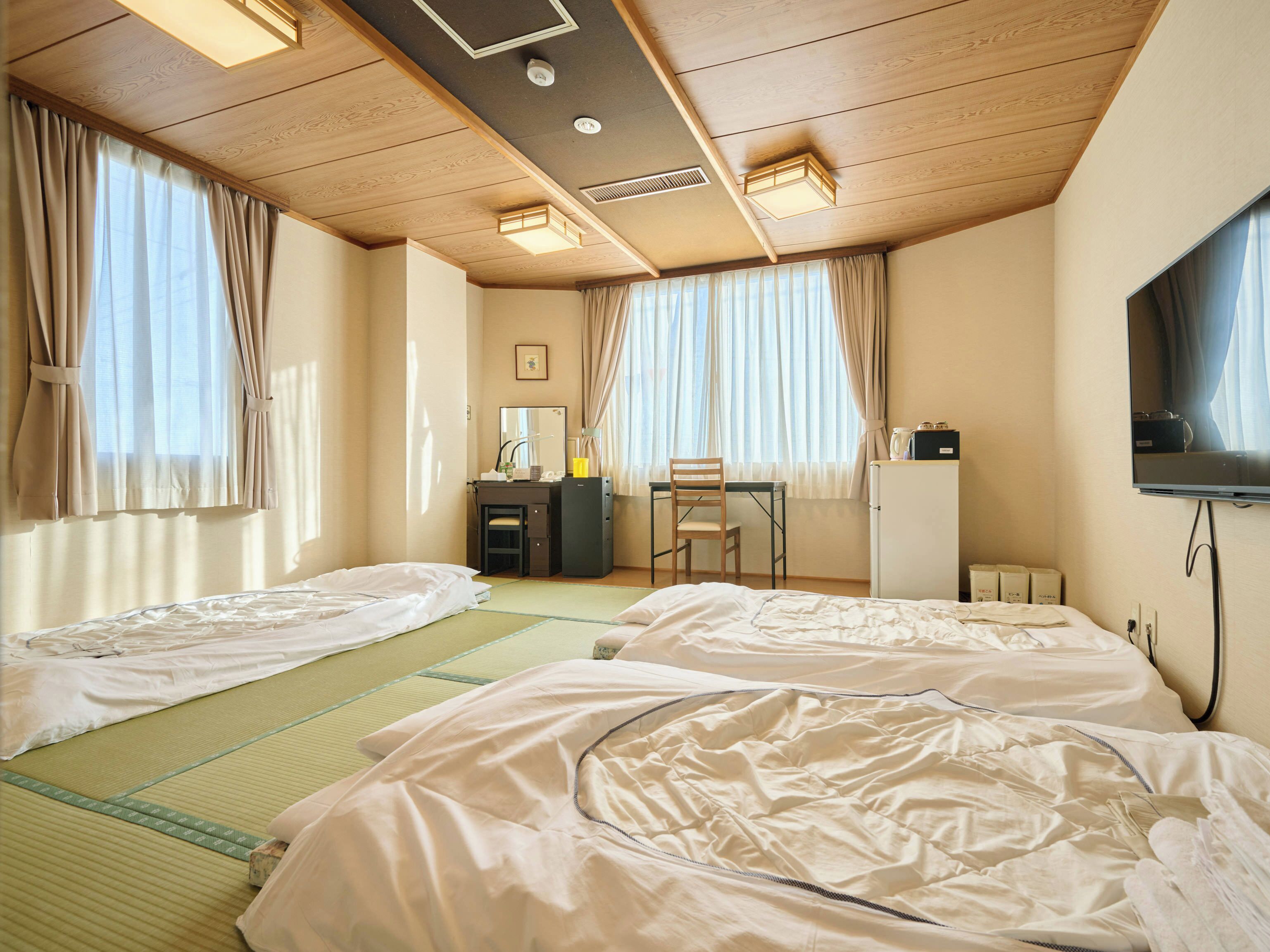 A hotel room with two beds, a desk, a chair, a television, and a wardrobe.