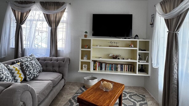 A living room with a grey sofa, a wooden coffee table, a bookshelf, and a ceiling fan. - Dolly’s Place perfect to unwind (Bayville)