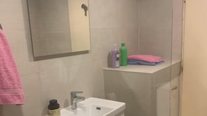 A bathroom with a white sink, mirror, and storage cabinet. There are toiletries on the counter and a shower area visible.