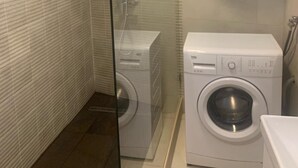 A modern bathroom with a glass shower enclosure, a built-in washing machine, and a wall-mounted water heater.