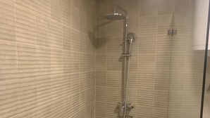 A small, tiled shower room with a glass door leading to a toilet area.