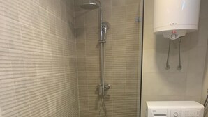A bathroom with a shower, toilet, and washing machine.