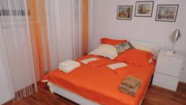 A neatly made bed with an orange bedspread, a white nightstand with a lamp, and three framed pictures on the wall.