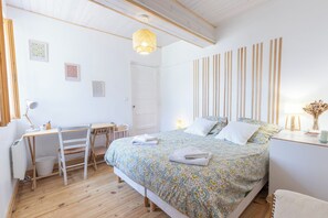 A bedroom with a bed, a desk, a chair, and a hanging light fixture.