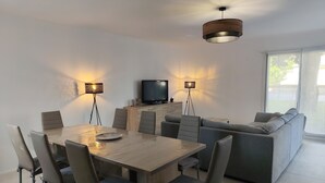 A modern living room with a dining area, a sofa, and a TV. - Gîte Le Magnolia (Ploërmel)
