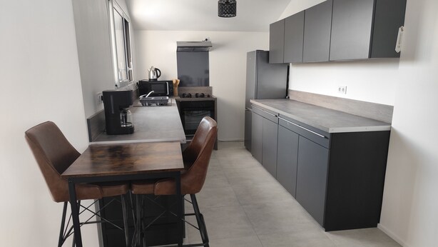 A modern kitchen with a central island, dark cabinetry, and a minimalist design. - Gîte Le Magnolia (Ploërmel)