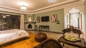 A spacious room with a large bed, a wooden coffee table with teapots, a television, and a fireplace.