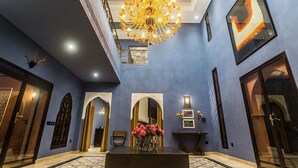 A grand lobby with a chandelier, arches, a reception desk, and a framed artwork on the wall.