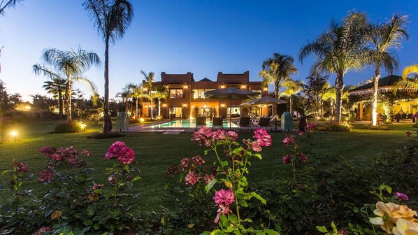 A large, two-story building with a swimming pool in the center, surrounded by lush greenery and palm trees.
