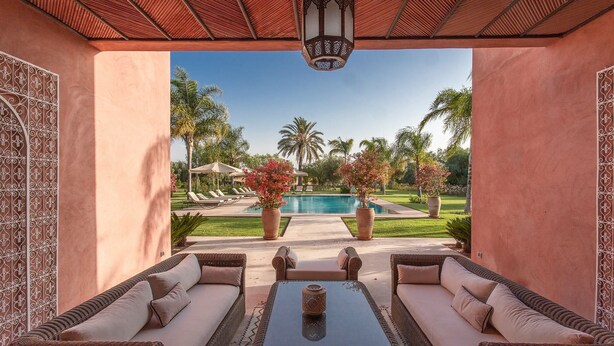 A covered outdoor seating area with a pool view, lounge chairs, and a decorative lamp.