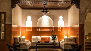 A cozy lounge area with a sofa set, two armchairs, a coffee table, and decorative wall sconces. - My Rental Homes | Riad Special with two courtyards and  swimmingpool (Marrakesh)