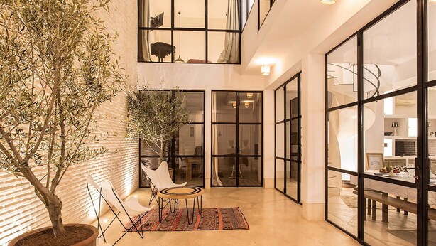 A spacious indoor area with a potted tree, a small round table, and a patterned rug. - My Rental Homes | Riad Special with two courtyards and  swimmingpool (Marrakesh)