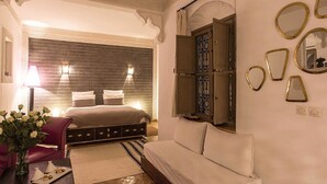 A bedroom with a large bed, a sofa, a small table with a vase of flowers, and a wall with decorative mirrors. - My Rental Homes | Riad Special with two courtyards and  swimmingpool (Marrakesh)
