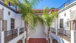 A courtyard with a central pool, surrounded by buildings with balconies and decorative iron railings. - My Rental Homes | Riad Special with two courtyards and  swimmingpool (Marrakesh)