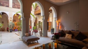 A spacious living area with a sofa, ottoman, and coffee table, surrounded by arches and potted plants.