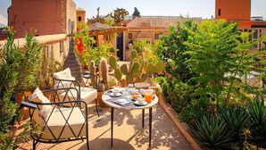 A rooftop patio with a table set for breakfast, surrounded by cacti and other plants.
