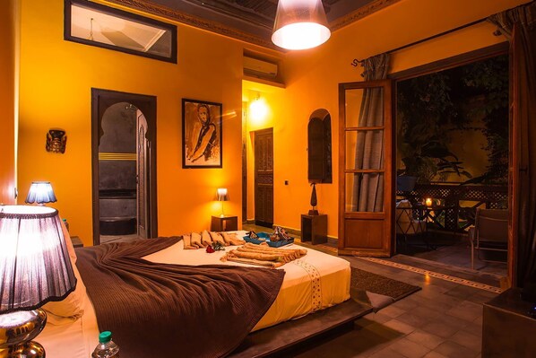 Una habitación con cama, lámparas de noche, un cuadro enmarcado y una puerta que da a un balcón.