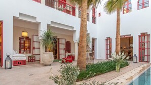 Um pátio com piscina, palmeiras e um edifício vermelho e branco com varandas.