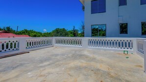 Eine Dachterrasse mit weißer Brüstung, einem Betonboden und einem Gebäude mit zahlreichen Fenstern im Hintergrund.