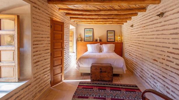 A narrow hallway leading to a bed with a wooden headboard, a wooden chest, and a patterned rug. - My Rental Homes - Villa Royale with pool and garden (Marrakesh)